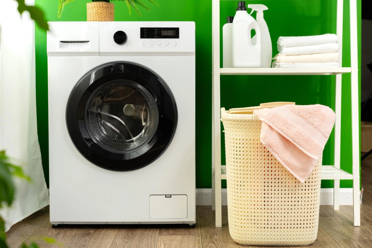 Máquina de lavar inverter em lavanderia moderna com cesto de roupas e produtos de limpeza sobre prateleira.